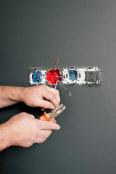 Close-up of an electrician using insulated pliers to install a flush wall-mounted socket and switch.
