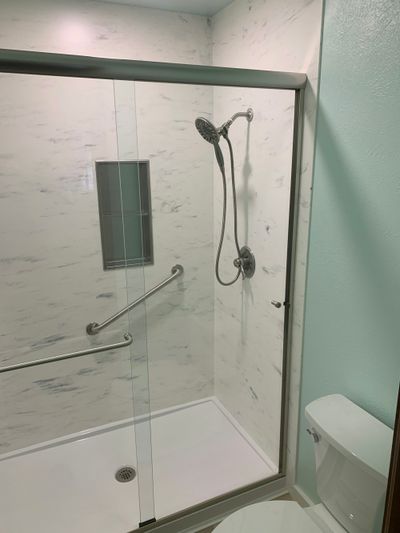 Walk-in shower fitted into a tiled bathroom with downlights illuminating the cubicle.